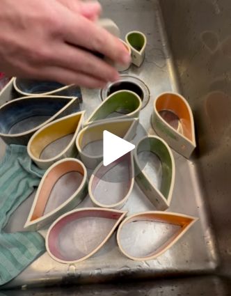 Colorful teardrop-shaped ceramic planters soak in a stainless steel sink as a hand sands the edge of one piece using a DiamondCore sanding pad.