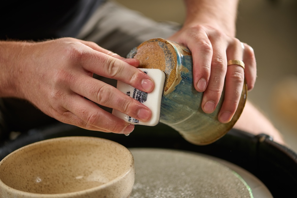 A man sanding the bottom of a glazed mug with a Flexible Diamond Sanding Pad