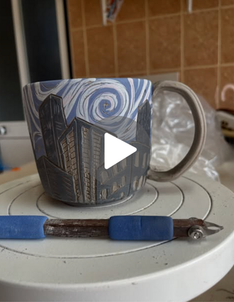 A mug featuring cityscape sgraffito designs stacked on a banding wheel, with a DiamondCore® carving tool in the foreground. The mugs feature swirling fall skies in rich, moody hues.