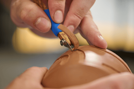 Hands with a tool carving on a piece of clay