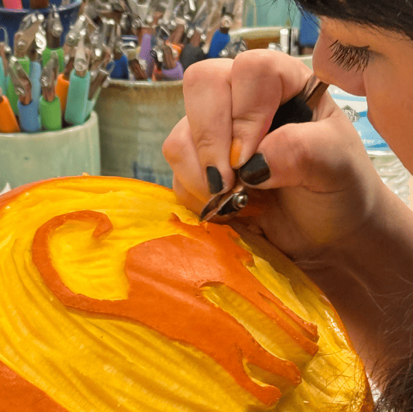 A woman carving a cat on a pumpkin with one of the DiamondGore Set tools